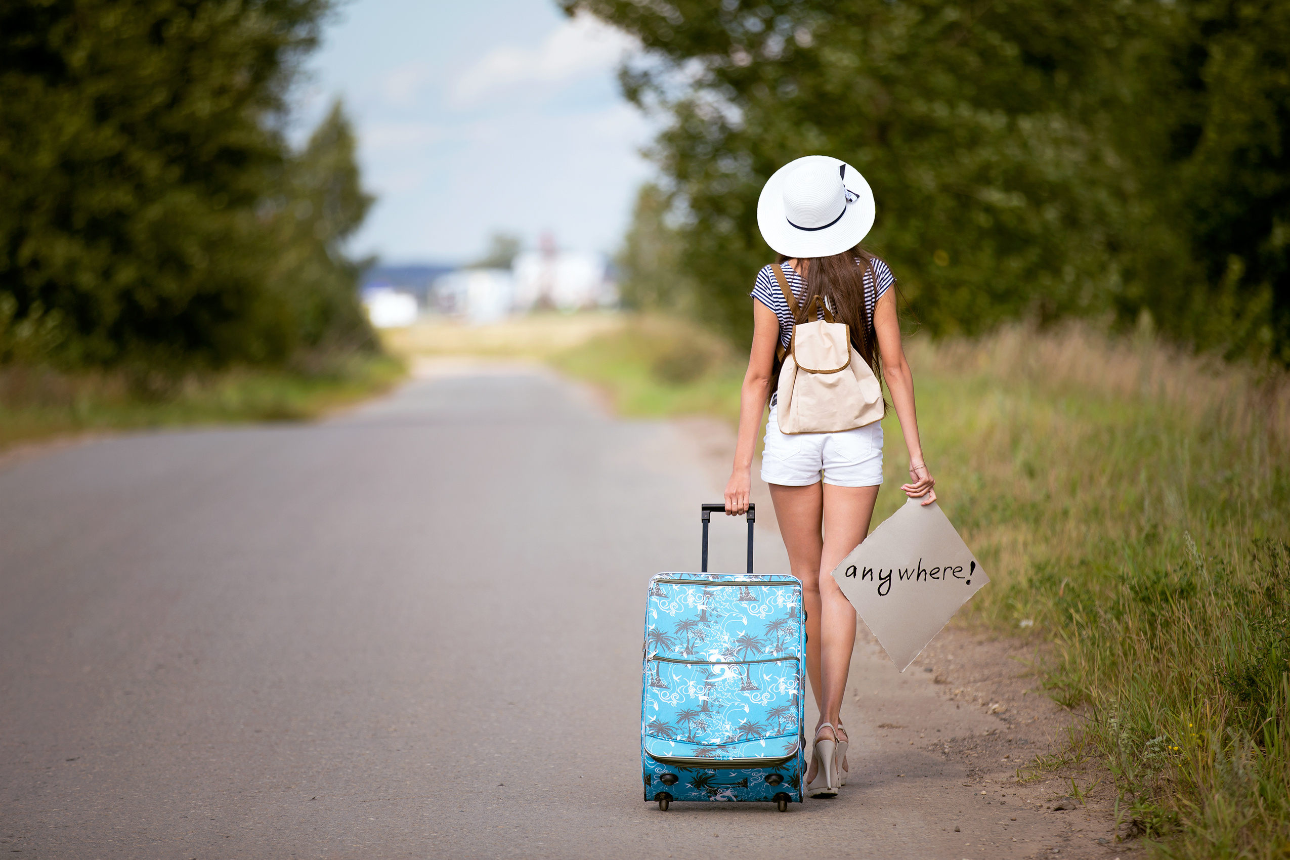 sexy brunette woman in shorts , t shirt and white hat with bag and backpack go on the road